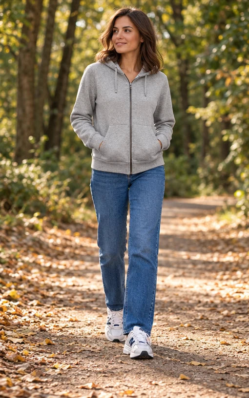 Une femme adulte portant Sweat Under Armour gris femme, Jean Replay bleu femme, Baskets New Balance blanc femme. Promenade d’automne. Mise en scène IA illustrative.