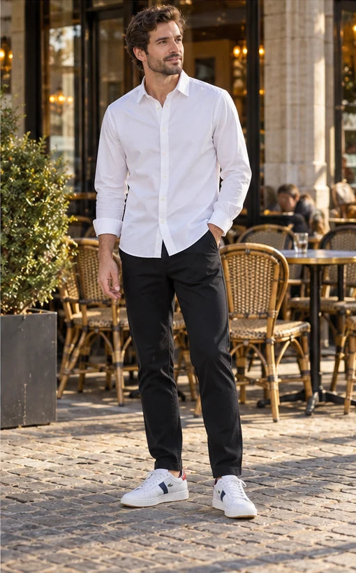 Un homme adulte portant Chemise Armani Exchange blanc homme, Pantalon Calvin Klein Jeans noir homme, Baskets Lacoste blanc homme. Une pause en terrasse. Mise en scène IA illustrative.